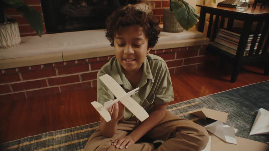 A boy sitting cross legged on the floor playing with a wooden model airplane