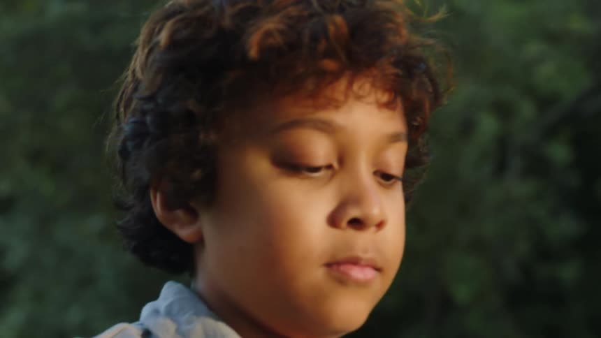 Boy picks paper plane up from lawn and brushes it off