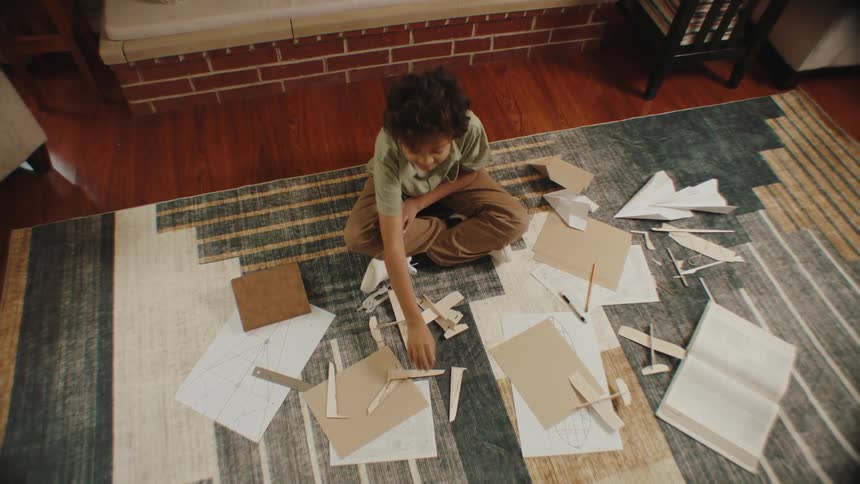 A boy making toy paper planes in the living room