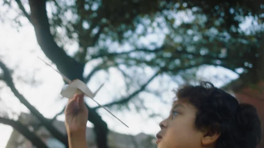 A boy plays with and throws a wooden toy airplane then runs after it