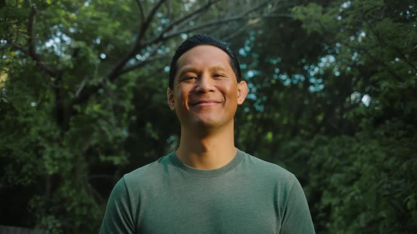 Portrait of a man in an outdoor environment with trees in the background smiling