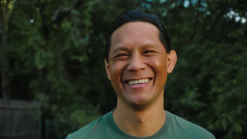 A man laughing while standing outdoors in a yard