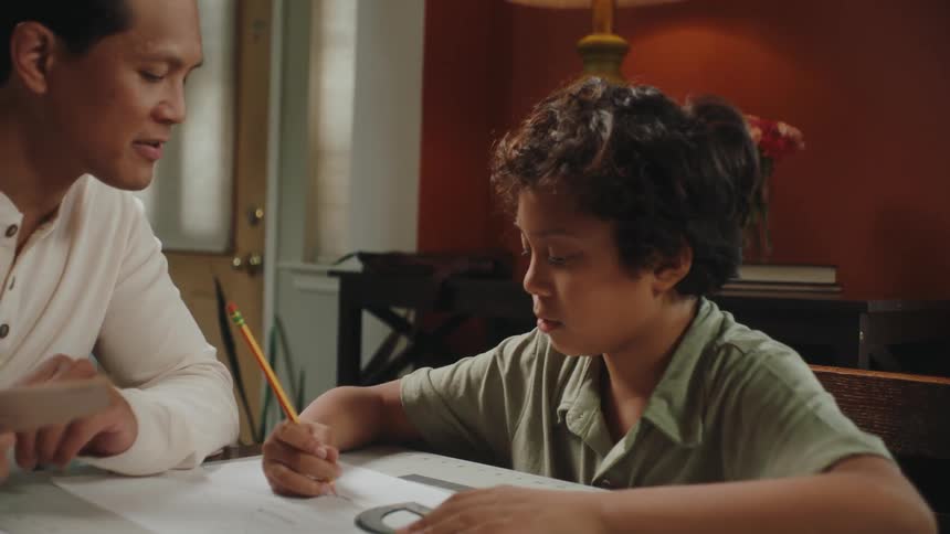 Boy sitting at the table with his father drawing a project