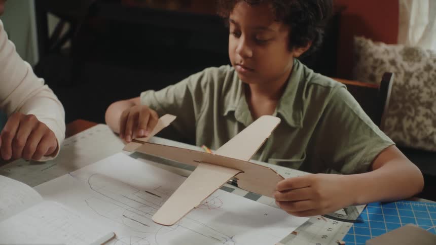 A young boy slowly assembles a cardboard plane