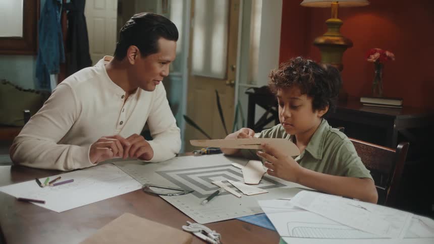 Father and son making toy paper planes in the living room