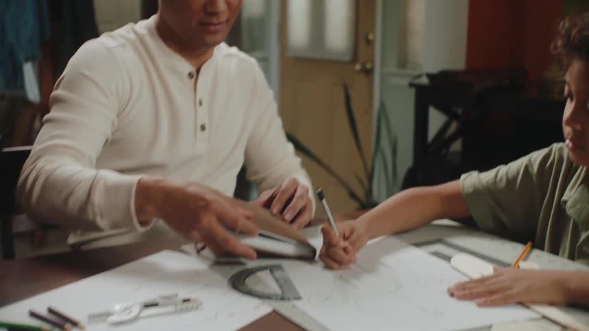 Father and son sitting at a table drawing a project on cardboard
