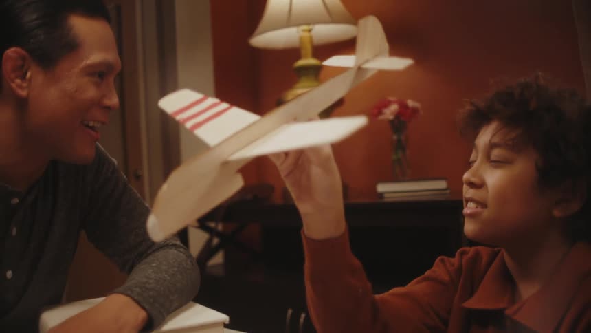 A father and son sitting at a table make a wooden airplane and have a conversation