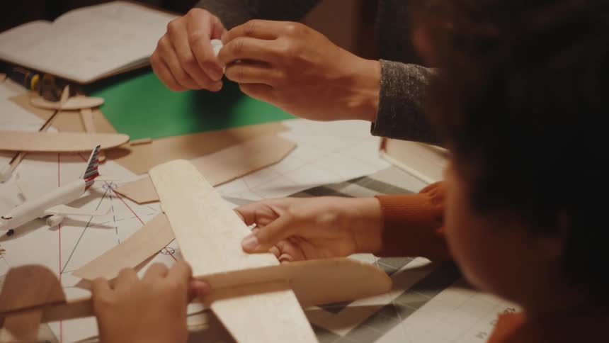 A man and a boy putting together a model airplane made of wood