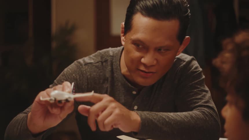 Father sitting with his son at the table showing a toy plane taking off