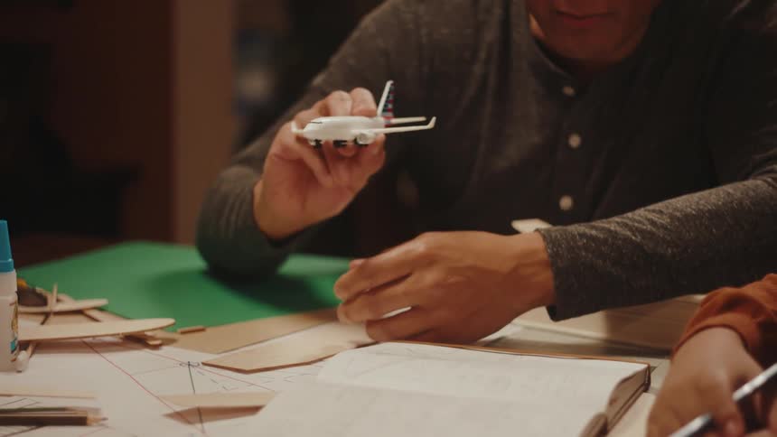 Father holding a toy airplane to his son while they are sitting at a table with books
