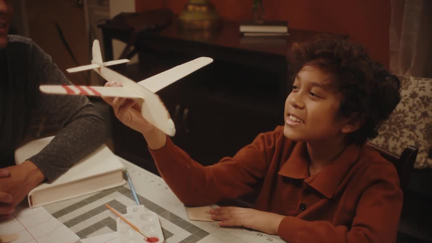 Father and son making toy paper planes in the living room