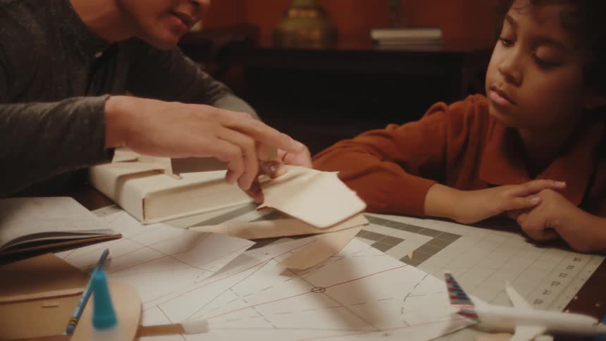 Father and son sitting at a table and using small pieces of wood building a project