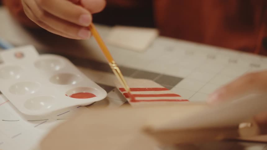 A boy smiling while painting the wing of a wooden airplane toy