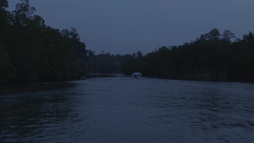 A lake that has a lot of waves due to a boat passing by and trees on the sides of the river