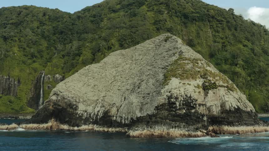A rock formation in front of a large island that is surrounded by water and a bird flying close to it