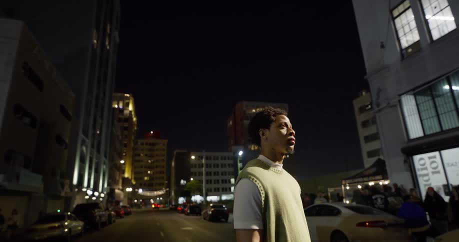 Man stands in street at night while a crowd waits near a building in the background