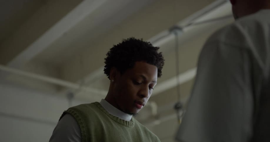 Tailor with curly hair wearing a white sweatshirt and a green vest take measurements for a mans suit in a tailors shop