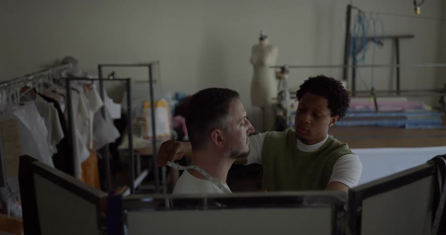 A black man takes measurements of a white man for making clothing