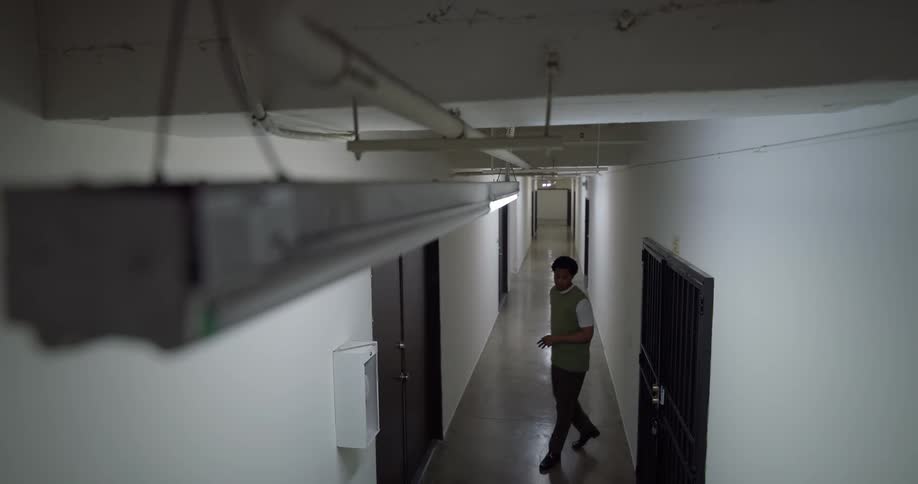 Man leaning against the wall of a corridor playing on his cell phone and then starts walking