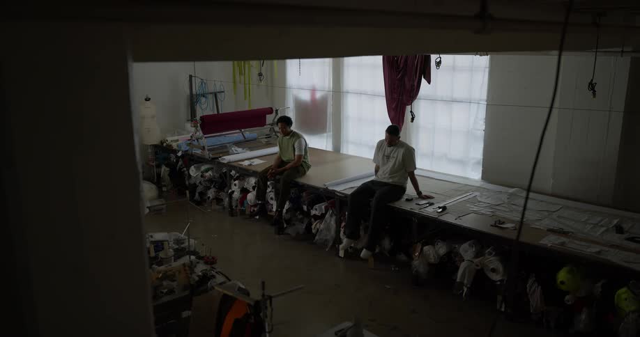 Two men are sitting at a huge table in a room and one of them is swinging his legs strongly