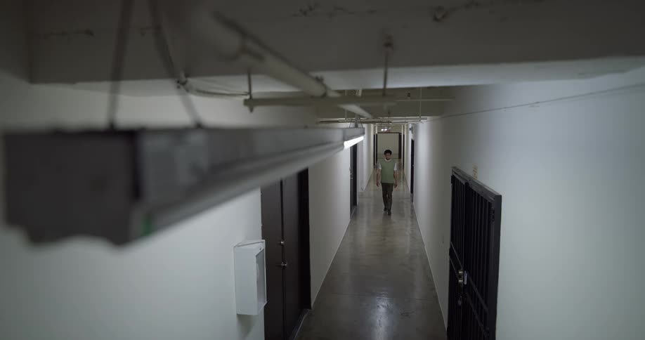 A person is walking down a hallway with white walls and black doors