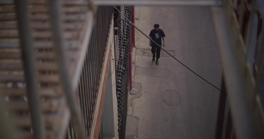 A lone male slowly walks along a concrete walkway past wrought iron fence
