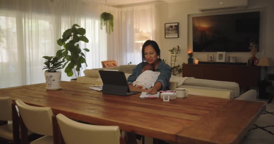 A mother sitting in front of her laptop and typing while holding her baby daughter in her lap
