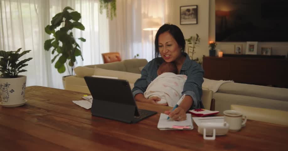 A mother holding her daughter in her lap while using her tablet and writing at the same time
