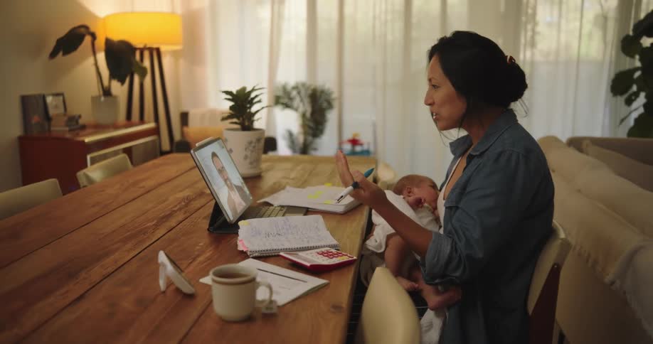 Mother carrying a baby while working from home talks on a video call