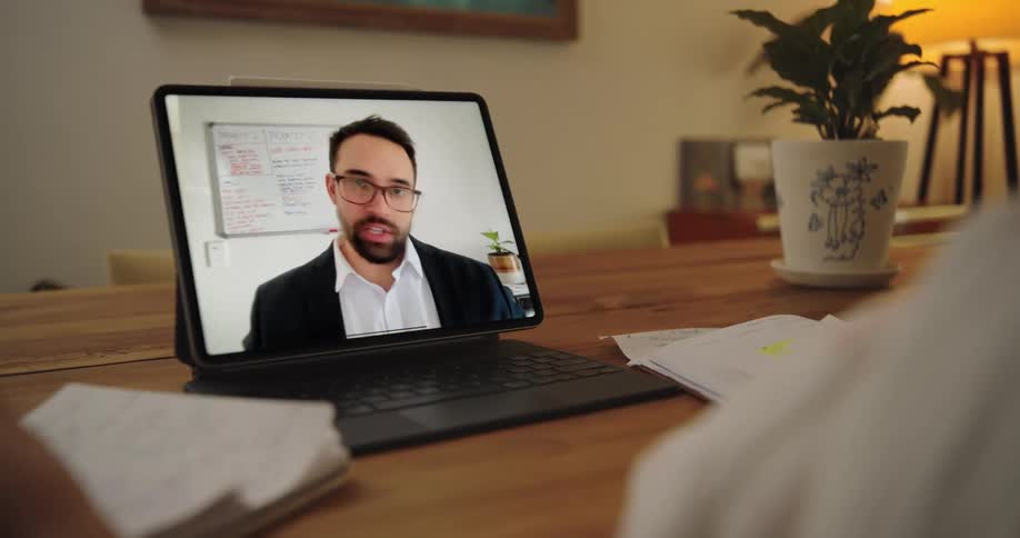A person on video call with a man on the tablet screen set on the table