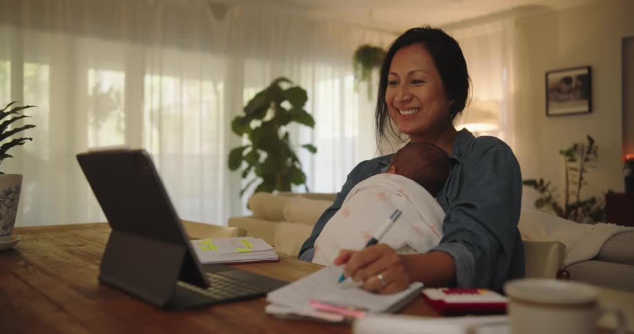 Mother holds baby while conversing via a video call from home