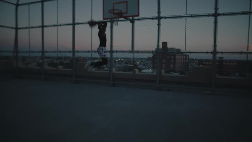 Man jumping and making a basket on a basketball court on the roof of a building