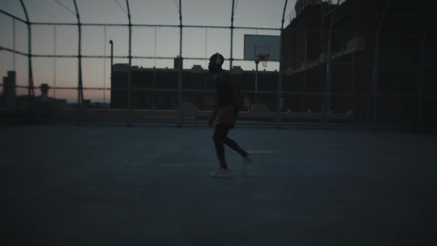 A man wearing white headphones plays basketball on the basketball court at dusk