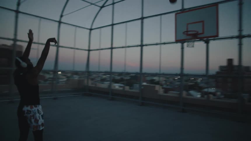 A black man is playing basketball on a court in an urban area