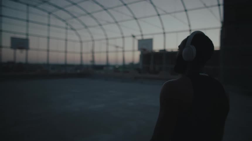 Man with headset carrying a basketball and entering the court on the terrace of a building