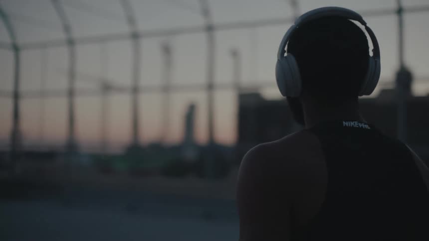 A black man with headphones walks a court while spinning a basketball on his finger