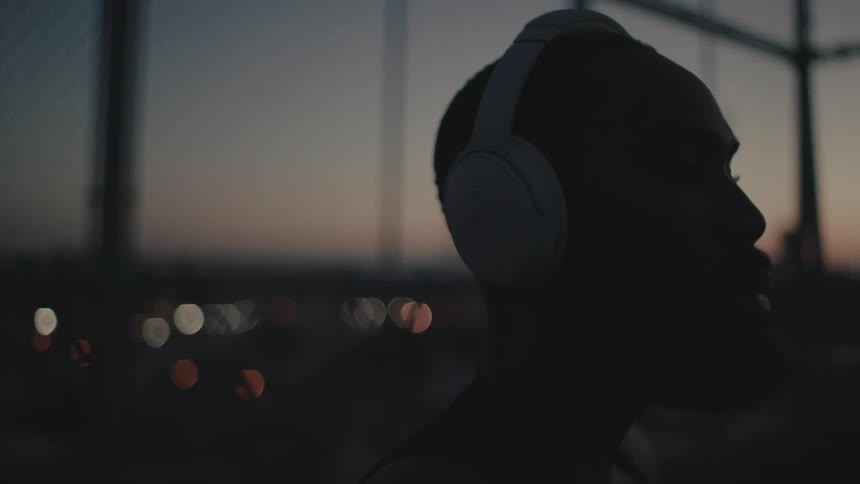 A man is wearing white headphones and shaking his head at night