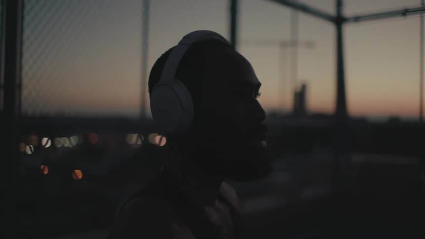 A man is wearing white headphones and is shaking his head and it is dusk