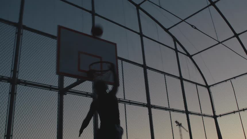 A silhouette of a man throwing a basketball and dunking it into the basket
