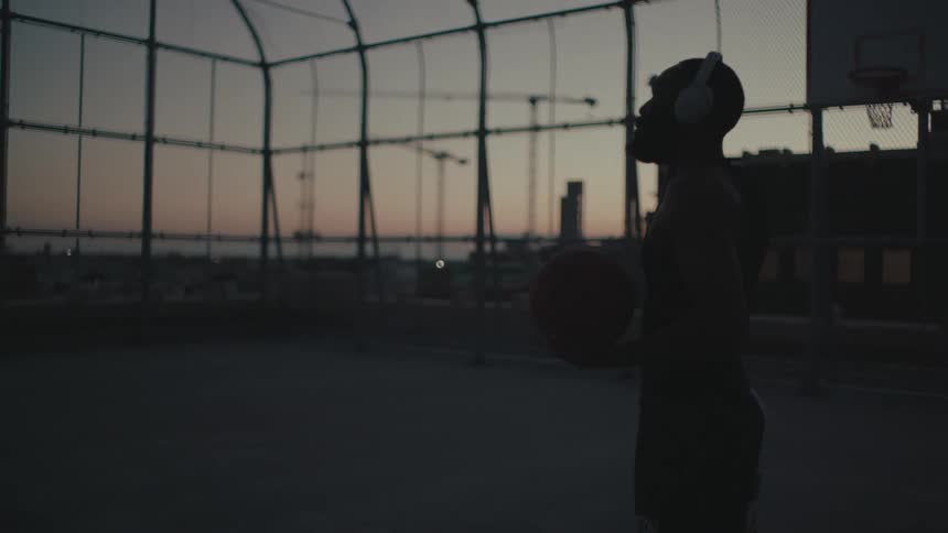 A black man drops a basketball on a court to adjust his headphones