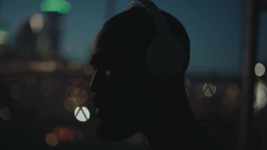Silhouette of a man wearing headphones against a backdrop of outoffocus city lights at night