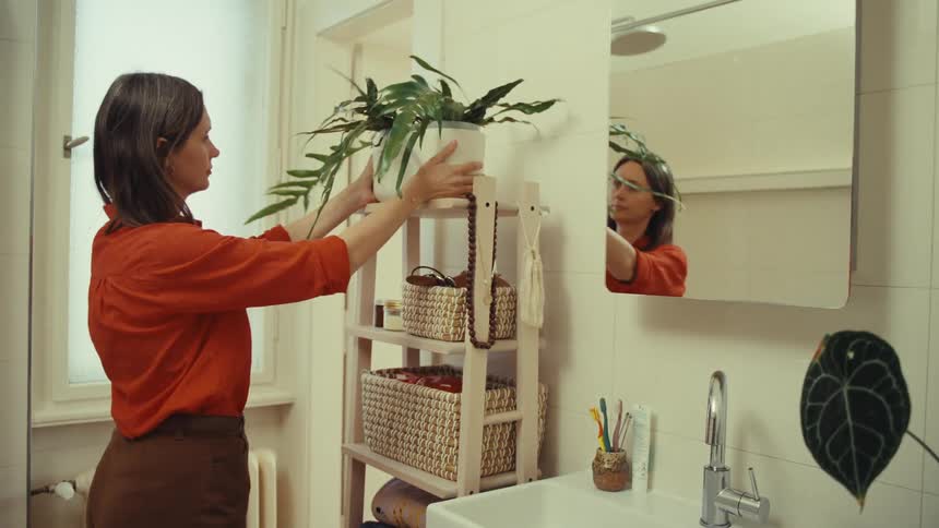 A woman in an orange shirt takes a plant from a pot and places it somewhere else