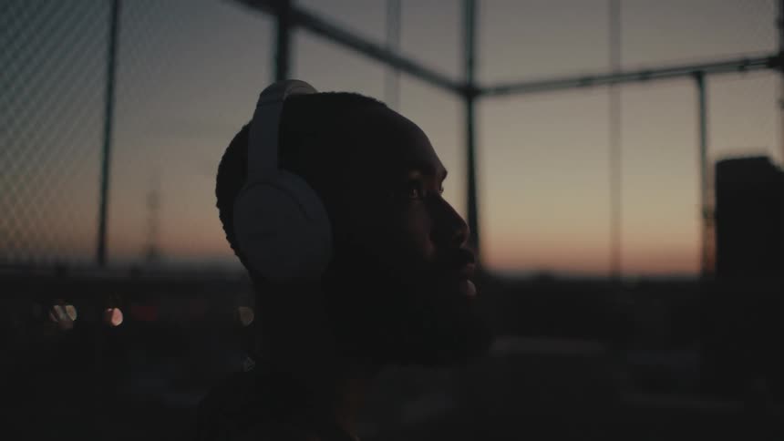 A bearded man wearing headphones listening to music on a basketball court