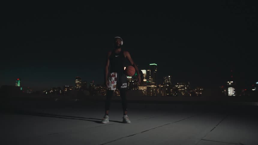 Basketball player holding a basketball stands against city skyline at night