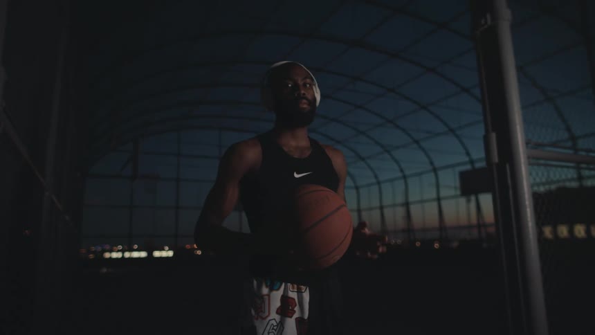 A man in headphones and a black tank top has a basketball in his hand and stretches it forward