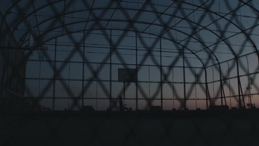 Man playing basketball while silhouetted against the sky makes a dunk