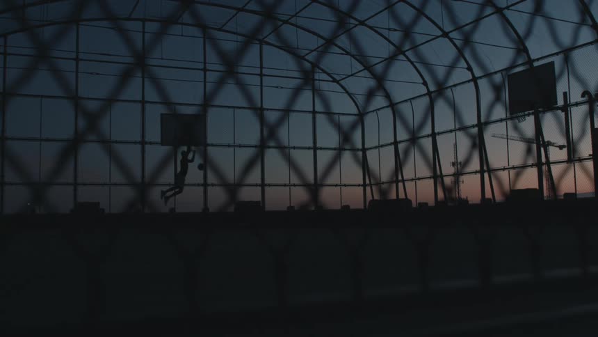 Man playing basketball is silhouetted against the sky at dusk