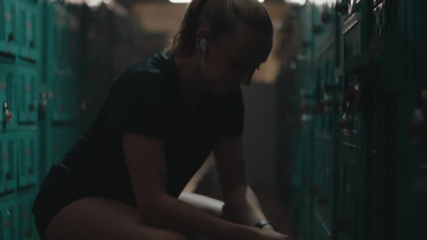 Woman sitting on a locker room bench with earbuds