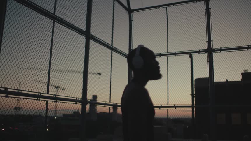 A black man listens to headphones on a court