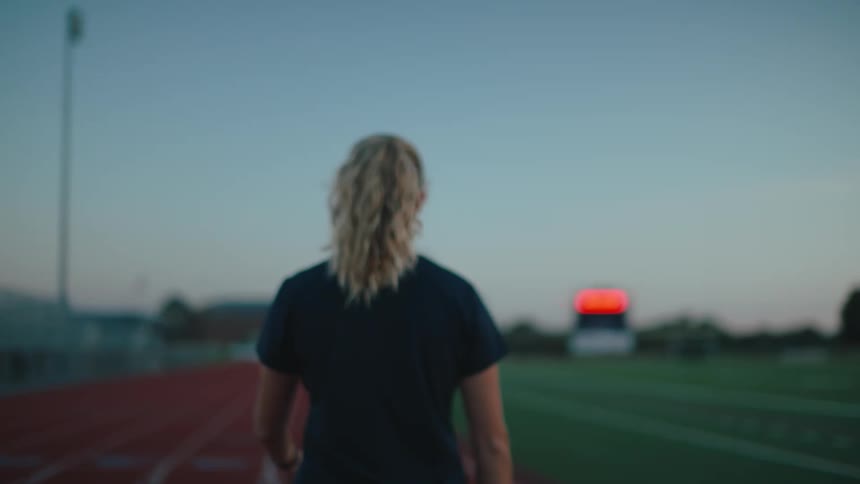 A woman with long hair walking on a track field during twilight